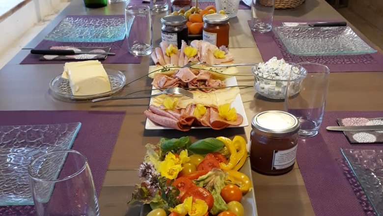 A laid breakfast table with cold cuts, vegetables, jam and drinks.