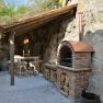 Rustic outdoor area with brick oven and wooden table under a wooden roof.