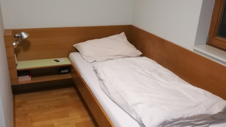 Single room with wooden bed, bedside table and lamp.