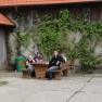 Four people sit at a wooden table in front of a building overgrown with ivy.