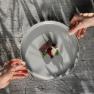 Two hands hold a plate with an artfully arranged gourmet dish above a wooden table.