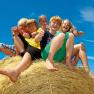 Group of young people sitting happily on a hay bale under a blue sky.