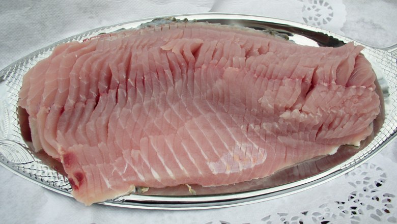 A raw carp fillet on a silver tray, surrounded by lace paper.
