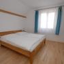A simply furnished bedroom with a double bed, wooden floor and a window with blue curtains.