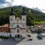 Aerial view of a church with two towers, surrounded by buildings and forest.