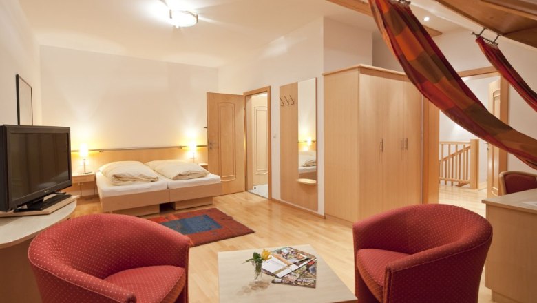 Cozy guest room with double bed, TV, red armchairs and hammock.