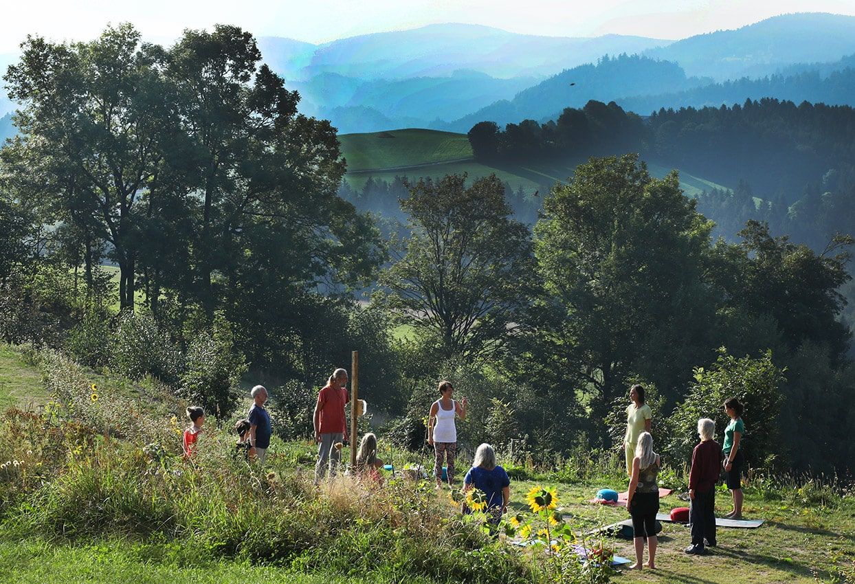 Group of people doing yoga outdoors in front of a picturesque mountain landscape.