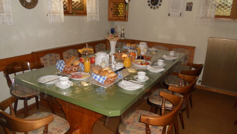 Frühstücksraum mit einem Tisch und Stühlen. Am Tisch ist ein umfangreiches Frühstück aufgedeckt.