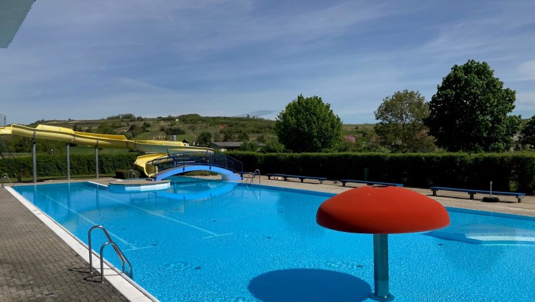 An outdoor pool with a yellow water slide, a blue pool and a red water feature in the shape of a mushroom.