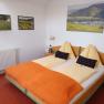 Cozy hotel room with double bed, orange ceiling and landscape pictures on the wall.