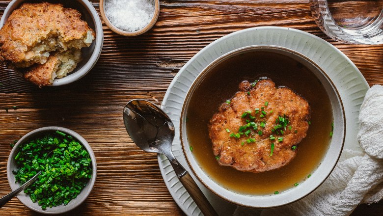 Cheese dumpling soup in a bowl on a wooden table, with chives and salt in small bowls next to it.