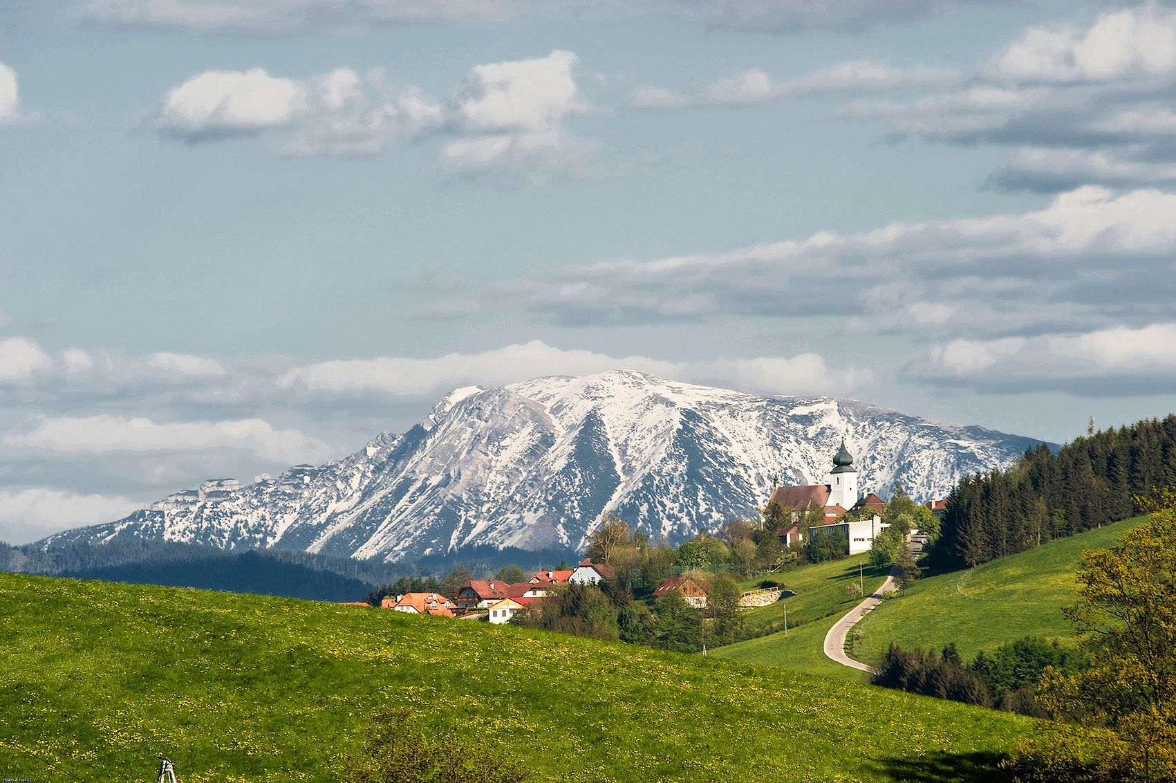 View of St. Leonhard am Walde with a snow-covered mountain in the background.