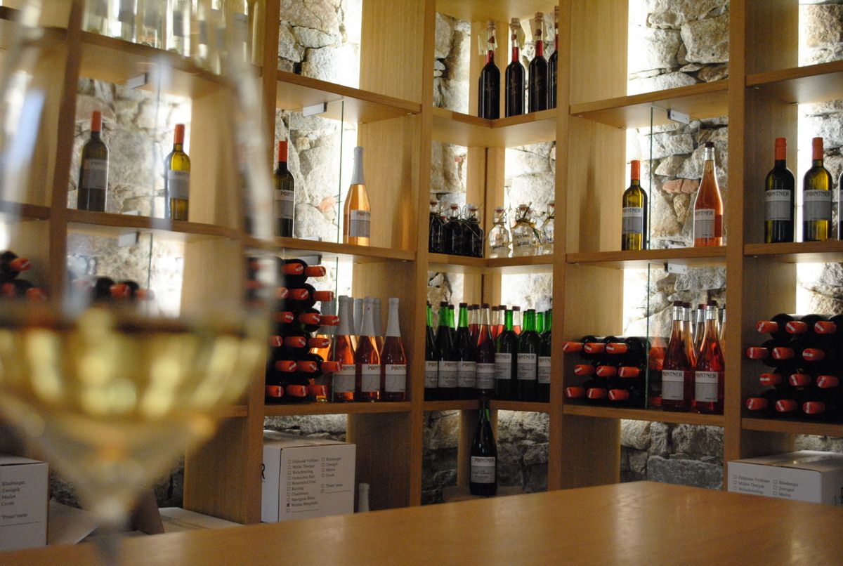 A tasting room with wine bottles on wooden shelves and a blurred wine glass in the foreground.