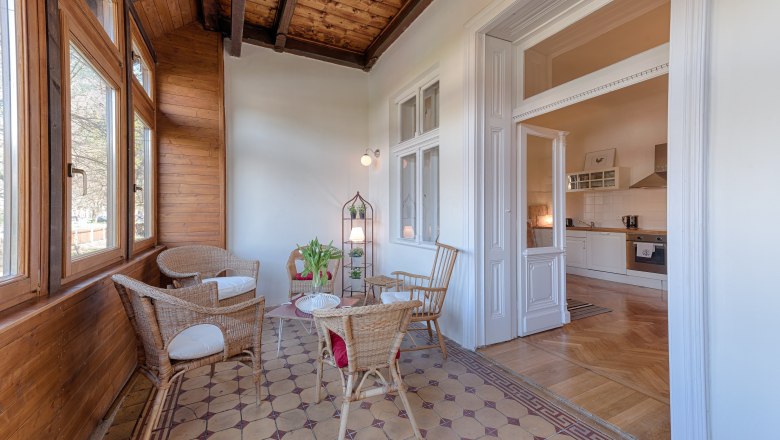Conservatory with wooden walls, rattan furniture and view into a kitchen.