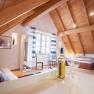 Cozy attic room with wooden beamed ceiling, bed, sofa, table and wine bottle.