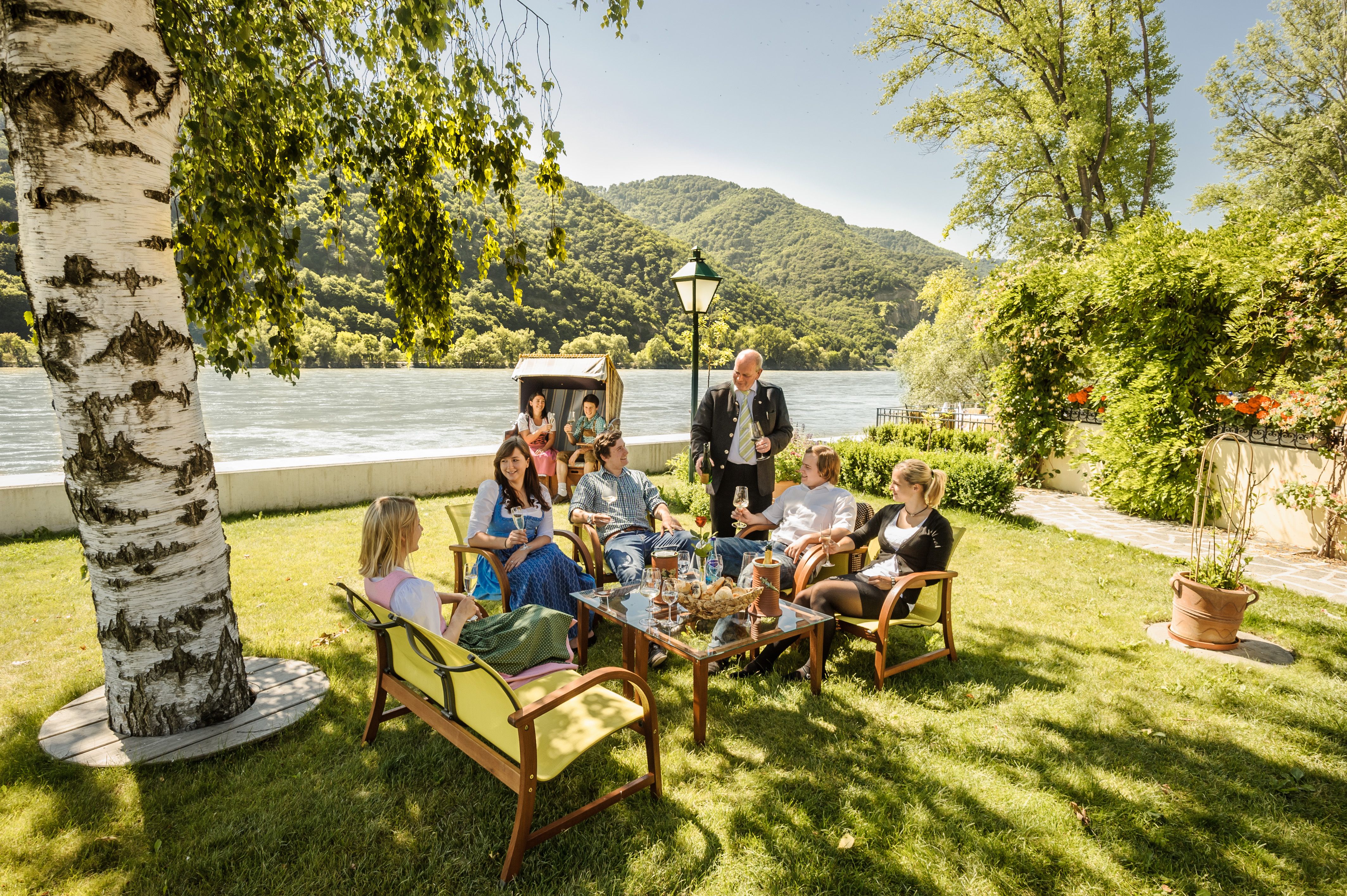 Group of people sitting in the garden of a restaurant on the riverbank.