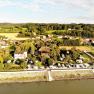 Aerial view of a campsite by the river with surrounding houses and green landscape.