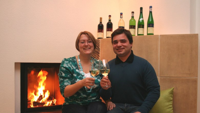 A couple is sitting in front of a fireplace, clinking glasses of wine.