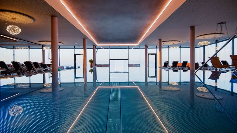 Indoor infinity pool, © Hotel Schachner_MIKU Media Interior view of an infinity pool with sun loungers and large windows.