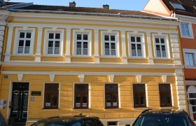 Yellow building with white window frames and decorative elements in Pöchlarn.