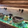 Modern bathroom with two stone washbasins on an illuminated glass table.