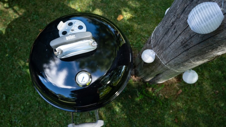 A kettle barbecue next to a tree trunk with fairy lights in the garden.