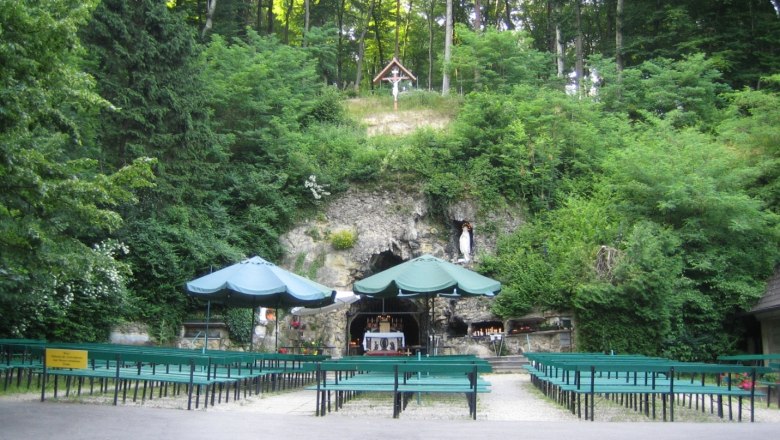 Lourdes grotto in the Vienna Woods with benches and green surroundings.
