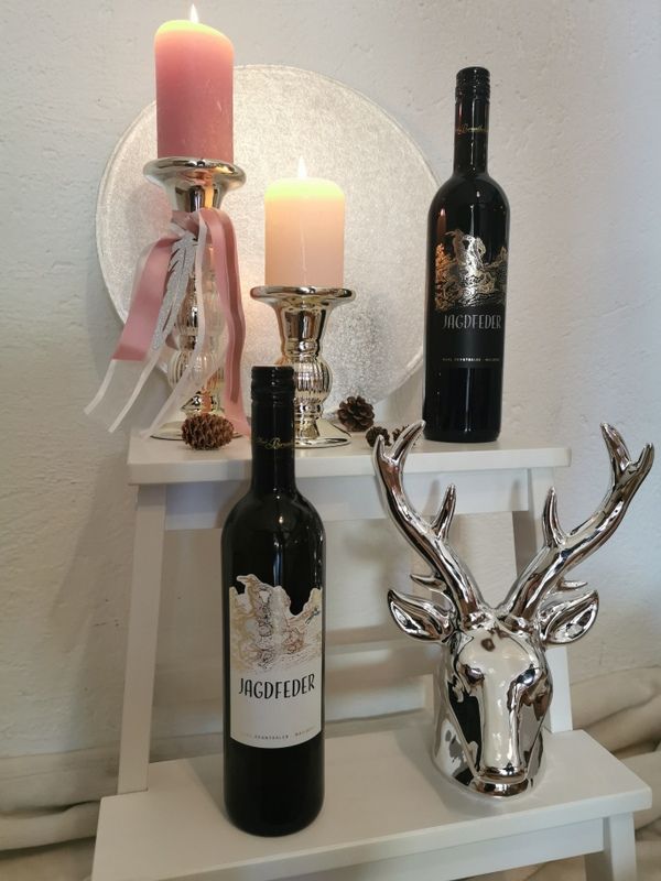 Two Jagdfeder wine bottles on a white shelf, decorated with candles and a silver stag's head.
