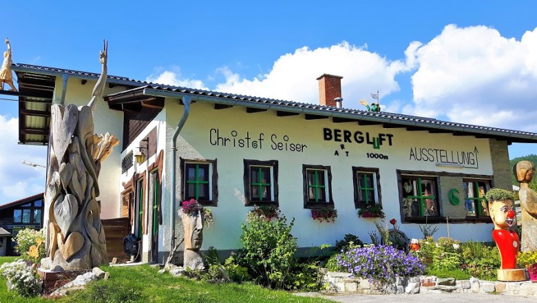 A building with the inscription 'Bergluft' and wooden sculptures in the foreground.