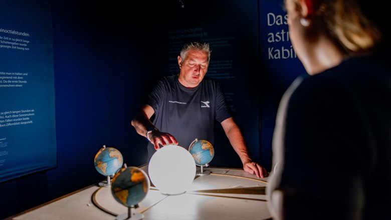 A man uses a model to explain the course of the sun in a dark room.