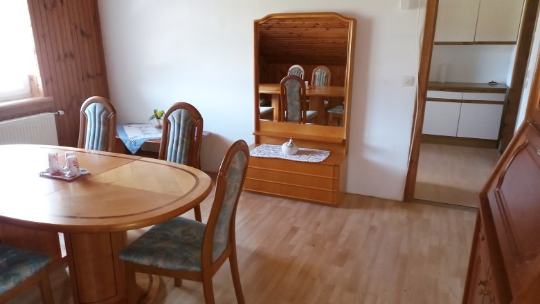 Dining room with wooden table, chairs and mirror, view into the kitchen.