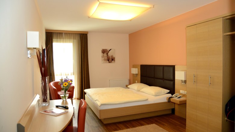 A modern hotel room with a double bed, desk, chair and bouquet of flowers on a table.