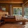 Rustic bedroom with wooden bed and large windows with a view of nature.