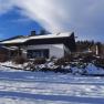 A snow-covered house in winter with a blue sky and trees in the background.