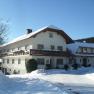 A large farmhouse covered in snow in winter, under a blue sky.