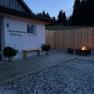 Terrace with fireplace and wooden fence at dusk, next to a building labeled 'Ferienwohnung Gutenberg'.