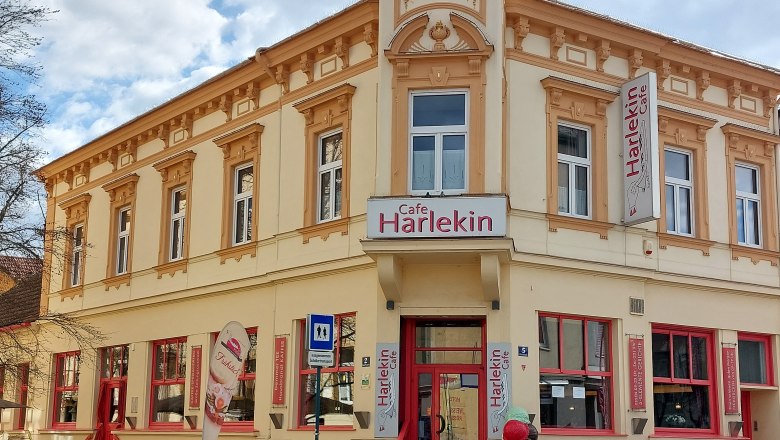 Exterior view of Cafe Restaurant Harlekin with yellow façade and red windows.