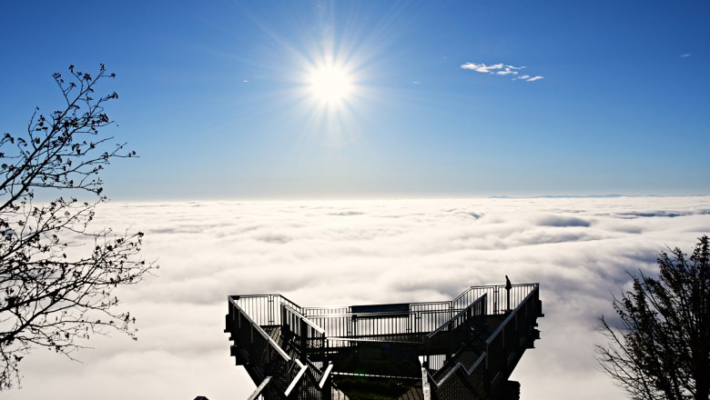 Viewing platform above a cloud cover with bright sun in the blue sky.