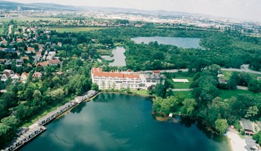 Aerial view of Brunn am Gebirge with a large building on the lake and a green landscape.