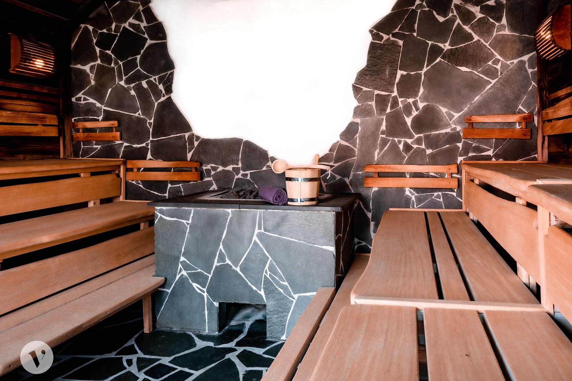 Interior view of a sauna with wooden benches and stone walls.