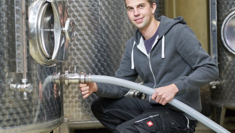 A man in work clothes kneels in front of a large stainless steel tank and holds a hose.