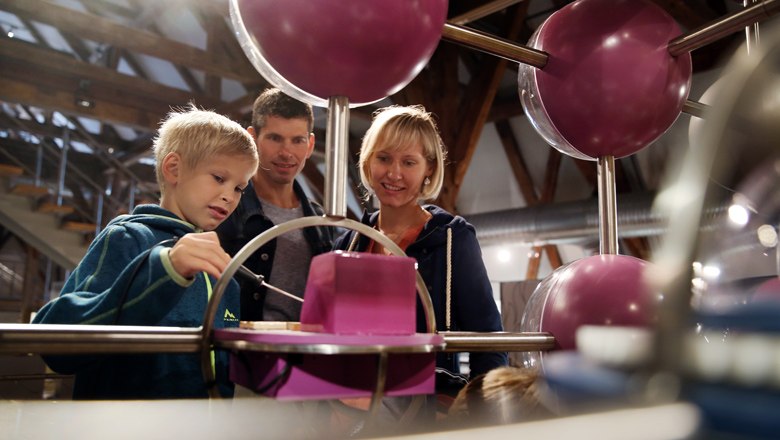 A family looks at an interactive exhibition with large, purple spheres.