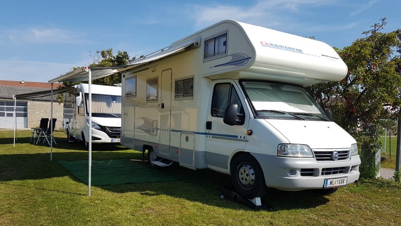 Motorhome, © Christa Kruspel A white motorhome with an extended awning is parked on a meadow next to another vehicle.