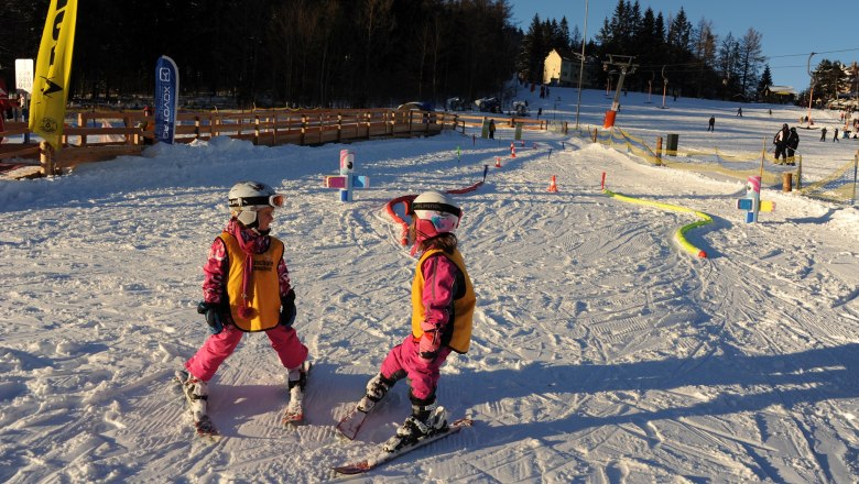 Two children in ski equipment in the snow, surrounded by colorful obstacles.