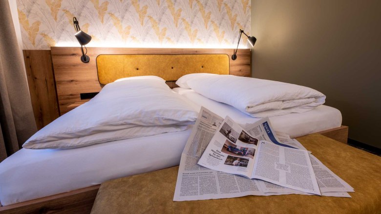 Cozy guest room with double bed, newspapers on the bedspread and stylish wallpaper in the background.