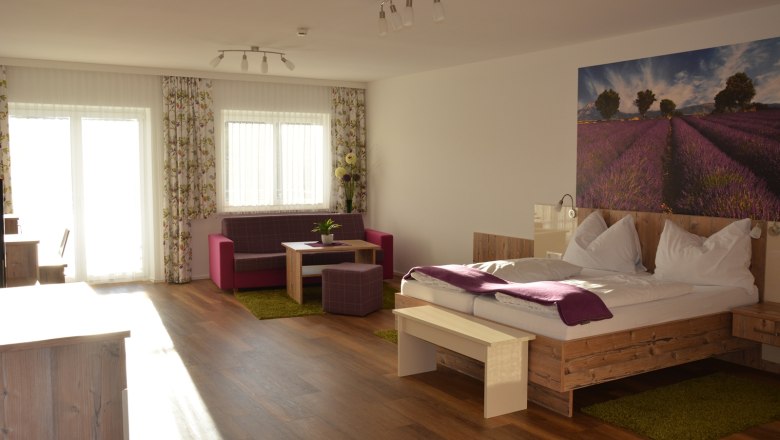A modern double room with a wooden floor, a large bed, a sitting area and a picture of lavender fields on the wall.
