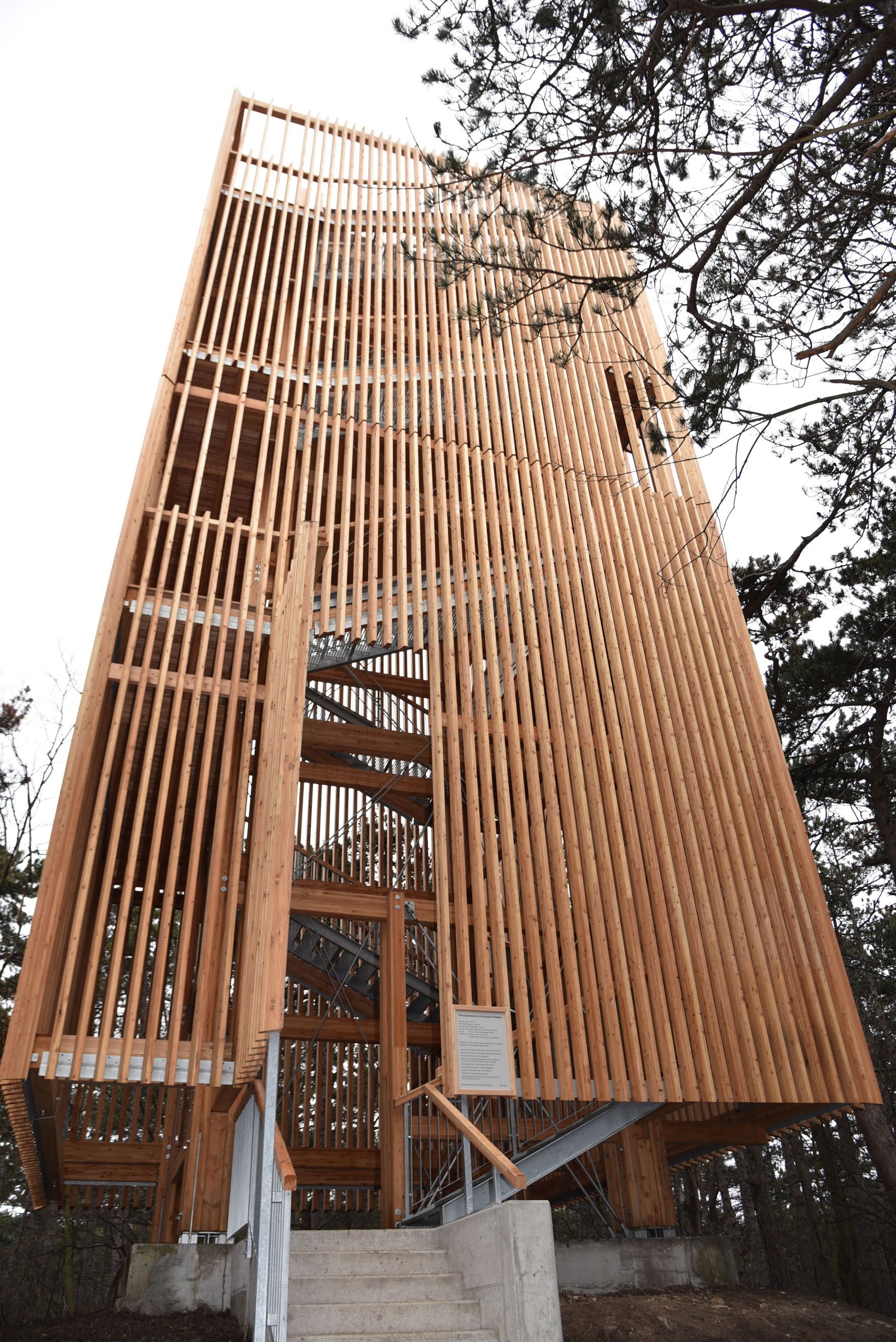 Wooden tower with vertical slats and stairs, surrounded by trees.