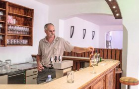 A man stands behind a wooden bar in a wine cellar and pours wine.