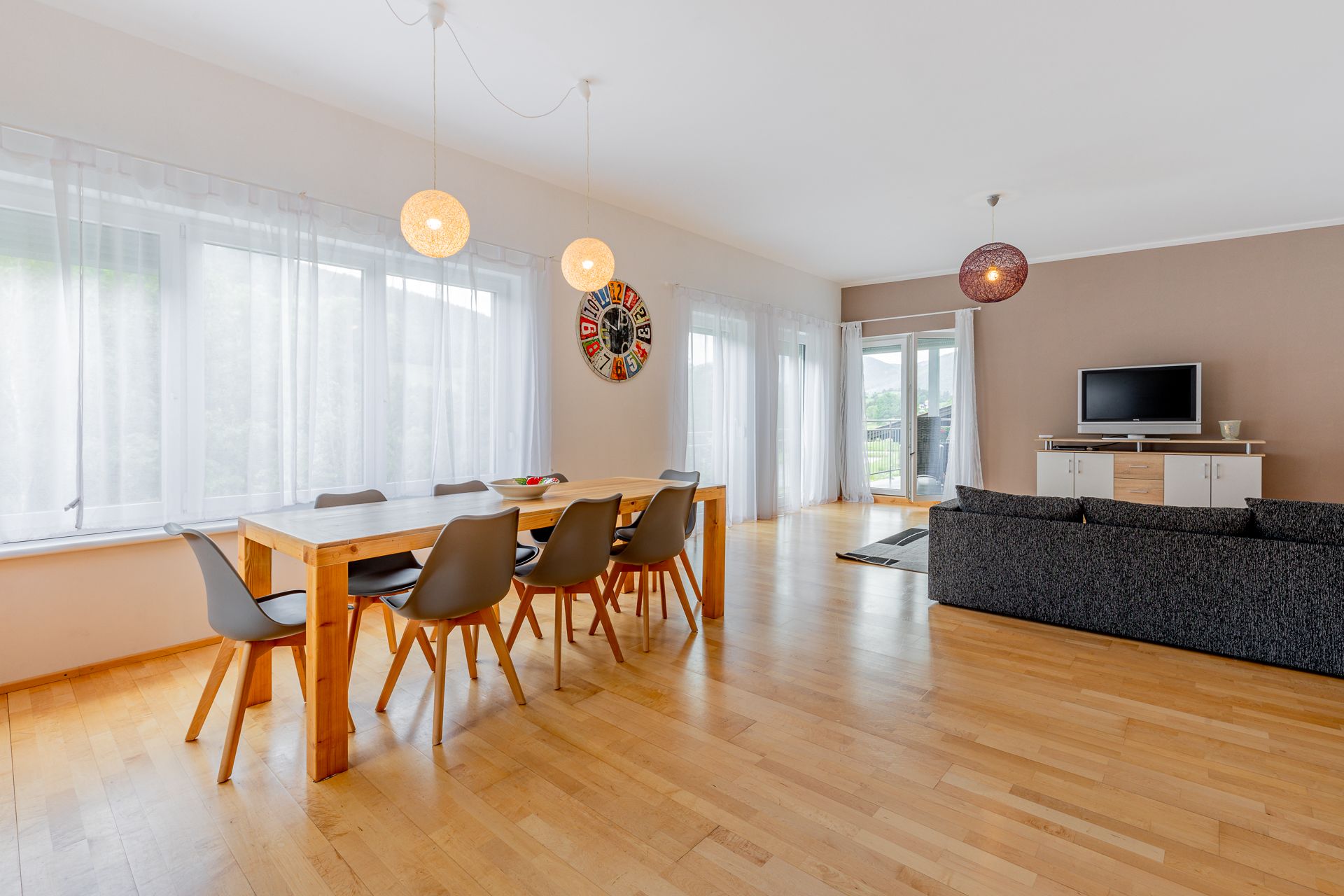 Modern dining area with wooden table, gray chairs and large window front.
