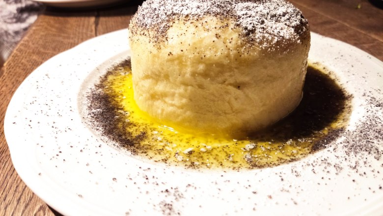 A yeast dumpling with poppy seeds and powdered sugar on a white plate.
